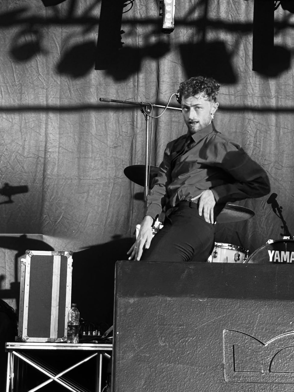Charlie Sin out of drag, dancing on stage in a dark shirt, in black and white