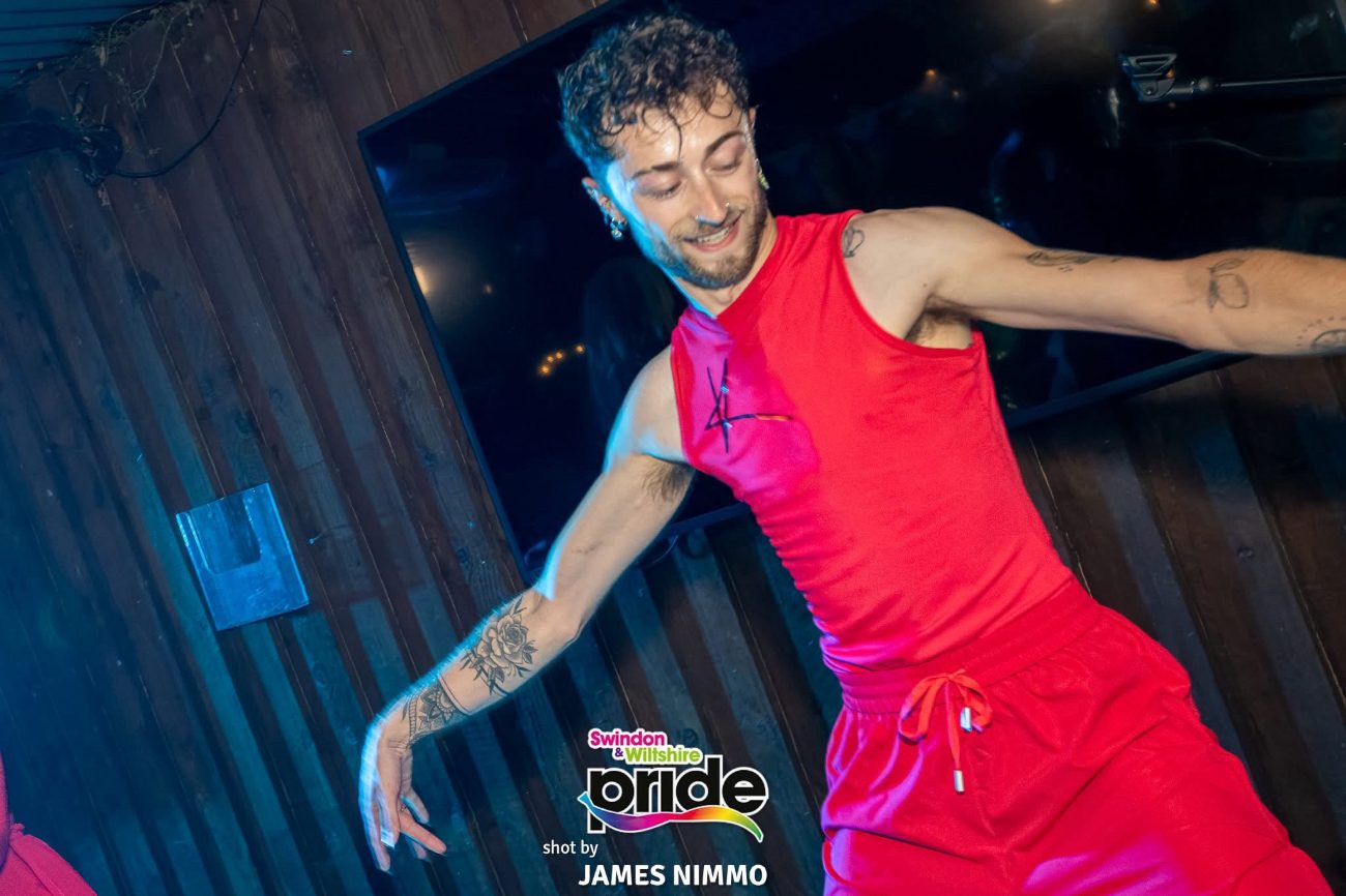 Charlie Sin dancing in a red sleeveless jumpsuit